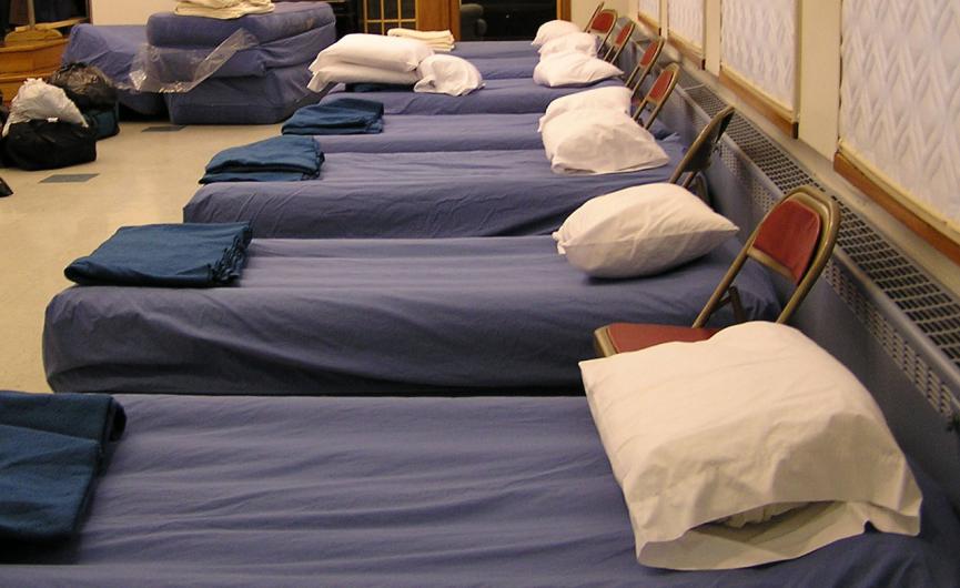 bed cots neatly set up next to one another in a homeless shelter